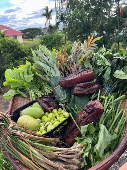 A basket overflowing with a fresh harvest from Nagaland. It contains smoked pork, wild greens, and local fruits, representing the bounty of the land that we bring to your plate in Mumbai.