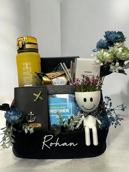 This personalized hamper for a brother named Rohan is packed with thoughtful items. It includes a travel wallet, a "World's Best Brother" frame, a quirky planter, a flask, and chocolates, all in a custom basket.