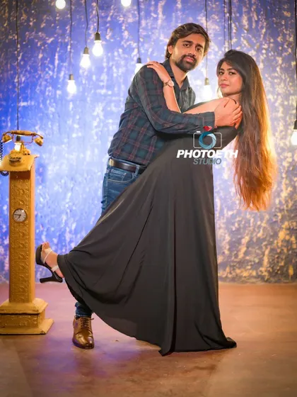 A stylish pre-wedding portrait against a textured blue wall with hanging lights. The vintage telephone prop adds a unique, retro touch.