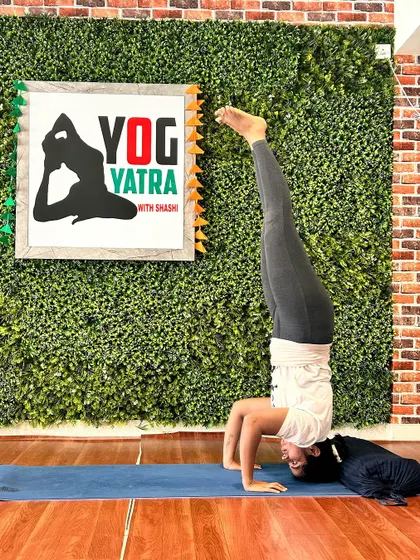 A student holds a steady Sirsasana (Headstand) with a dog playfully joining in, showcasing the fun and welcoming atmosphere of our studio.