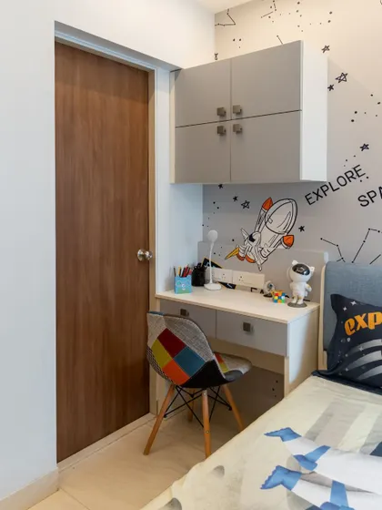 The compact study corner in the space-themed room, with a desk and overhead cabinets that provide ample storage for books and school supplies.