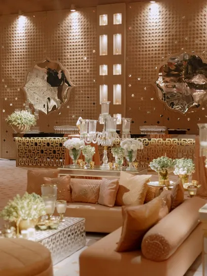 We designed this lounge area with a custom back wall featuring metallic panels and abstract mirrors. The setup includes a modern bar and comfortable seating, all in a cohesive pastel and gold color scheme.