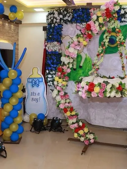 A creative naming ceremony setup with a 'baby's arrival' theme. The decor includes a floral swing for the cradle, a baby in a parachute cutout, and other cute elements to celebrate the new boy.