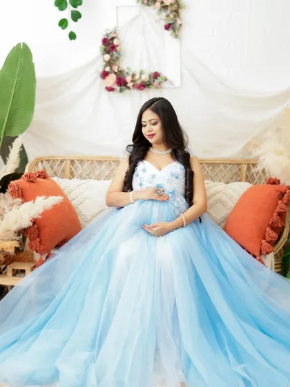 A serene portrait in a beautiful blue gown. The mom-to-be is seated in a cozy boho setting, her expression full of peace and happiness.