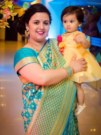 A mother in a beautiful turquoise saree holds her daughter in a yellow dress. We capture the vibrant colors and traditional attire at family events.