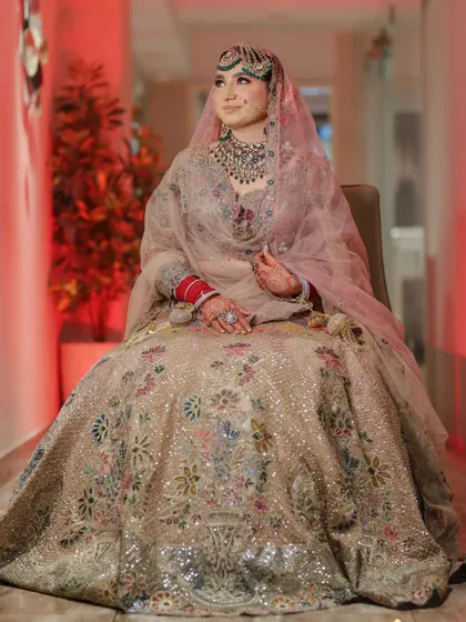 A full-length seated portrait of the bride, showcasing the beautiful embroidery of her lehenga.