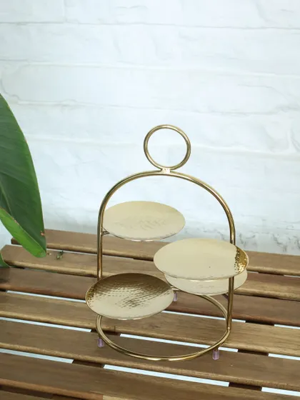 The Tête-à-tête stand, shown empty to highlight its elegant form. The three hammered gold plates are ready to be filled with your favorite treats for a stylish presentation.