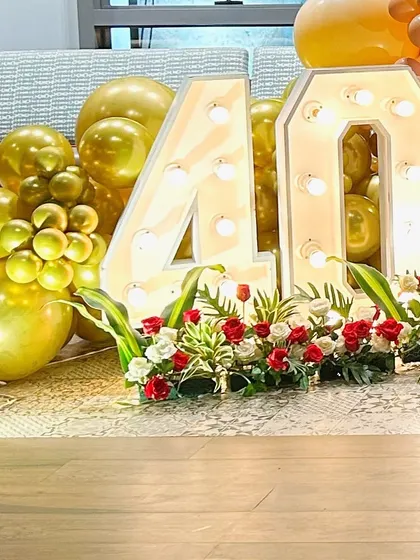 A close-up of a 40th birthday celebration, showing the large marquee '40' decorated with flowers and surrounded by gold balloons.