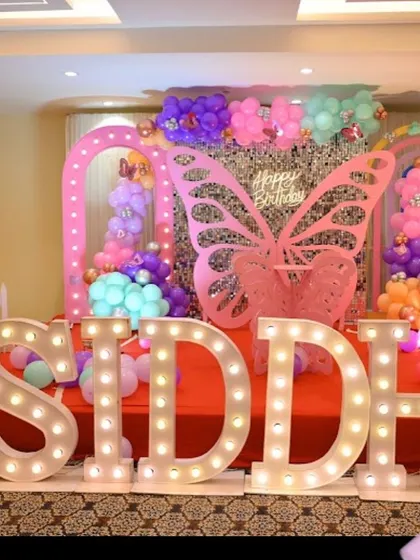 A full stage view of a butterfly-themed birthday for "SIDDHI". The setup includes multiple lighted arches, a central butterfly prop, and colorful balloon clusters.