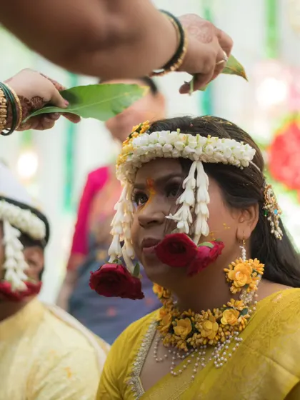A close-up of the bride during her Haldi ceremony as a family member performs a ritual with a mango leaf, a beautiful traditional moment.