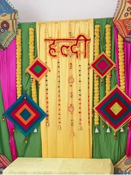 A colorful Haldi backdrop with green and yellow drapes, decorated with hanging kites and traditional umbrellas.