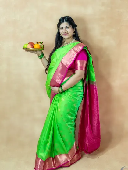 A traditional and graceful studio portrait of a mom-to-be in a green saree, holding a plate of fruit.