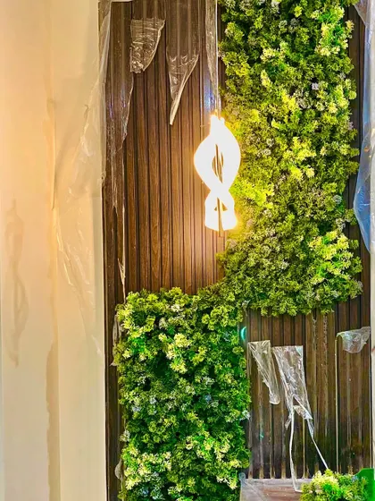 This custom installation features a flowing design of artificial moss and leaves on a wood-paneled wall, with a modern light fixture integrated directly into the greenery for a truly unique art piece.