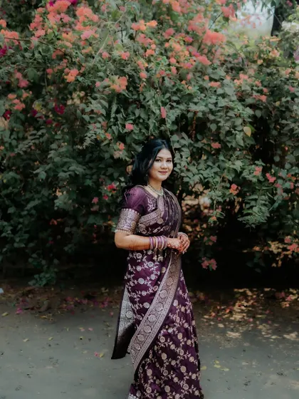 A full-length shot of the bride-to-be, showcasing her elegant purple saree against a natural, floral background.