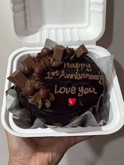 A decadent chocolate bento cake for a first anniversary, topped with KitKat pieces and chocolate swirls.