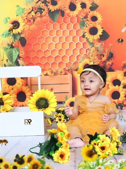 A close-up of the baby girl in the sunflower setup, looking curious and sweet. The warm, golden tones of the photo create a beautiful and heartwarming image.