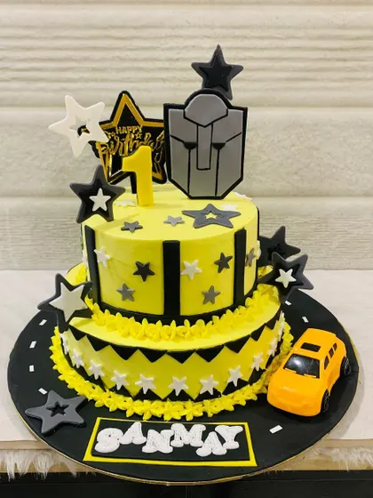 A cool two-tiered car-themed cake for a first birthday. The design features a road, stars, and a yellow toy car, perfect for a little vehicle enthusiast.