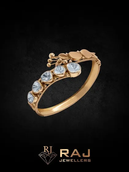 A simple yet elegant bangle featuring a row of large polki stones. A small, delicate floral charm adds a touch of whimsy to this classic piece, proving that beauty can be found in perfection.
