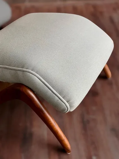A detail shot of the custom armchair's ottoman, focusing on the smooth, curved lines of the teakwood legs and the fine texture of the upholstery.