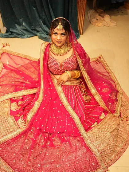 A bride seated gracefully, showcasing the full flare of her rani pink banarsi-style lehenga. The gold detailing and rich fabric exude royalty and tradition.