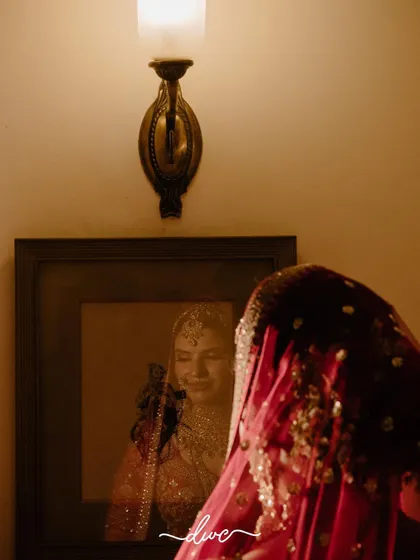 An artistic shot of the bride looking at her own reflection in a framed picture, a creative and contemplative getting-ready moment.