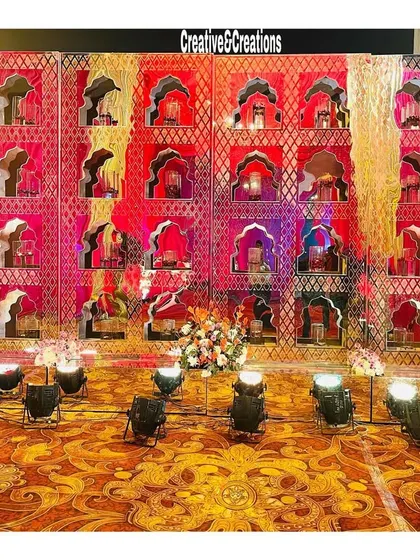 A stunning 'jharokha' wall lit with red and pink lights. This intricate backdrop can be used as a photo wall or part of a larger stage setup.