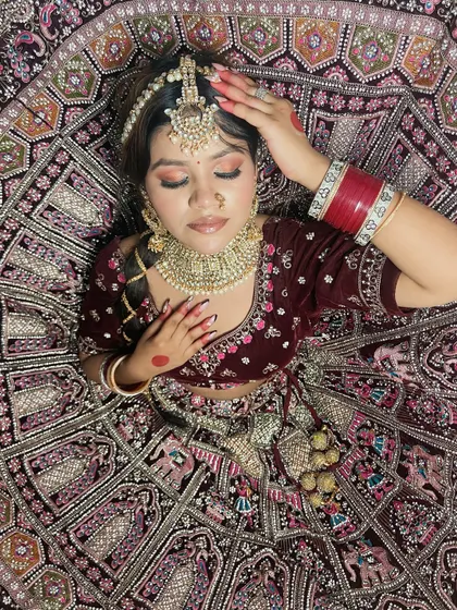 An artistic top-down shot of a bride in a deep maroon velvet lehenga. This photo highlights the hairstyle, makeup, and the beautiful spread of the embroidered skirt, a composition technique our students learn during portfolio shoots.