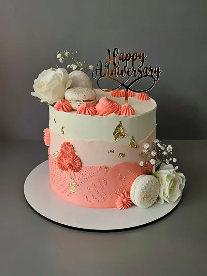 A peachy and coral anniversary cake. This chocolate truffle cake is decorated with macarons, fresh flowers, and gold leaf for a beautiful and elegant finish.