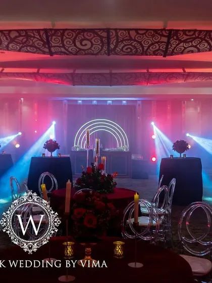 A bold and luxurious reception with a red and black color scheme. The decor includes rich red roses, modern crystal candelabras, and a stylish bar with a neon arch backdrop.