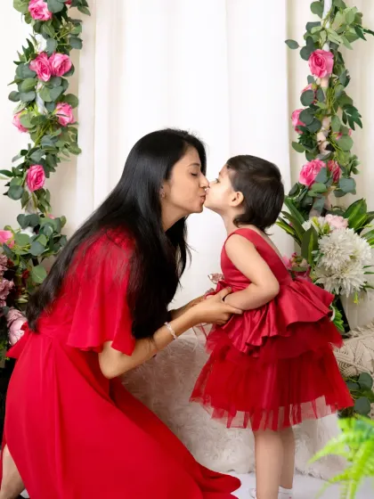 A sweet kiss between a mother and her daughter, both dressed in red, captured in front of our beautiful floral arch.