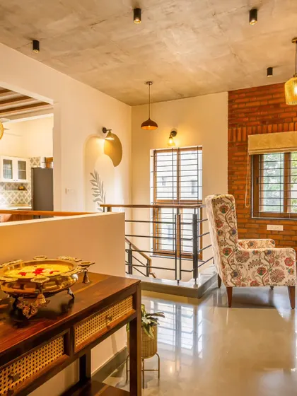 A wider view of the Akshaynagar duplex living area, showing the open-plan layout that connects to the staircase and kitchen. The mix of floral prints, cane, and wood creates a comfortable, eclectic vibe.
