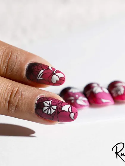 A client's hand showing a beautiful stamping art design with a floral pattern over a deep red ombre.