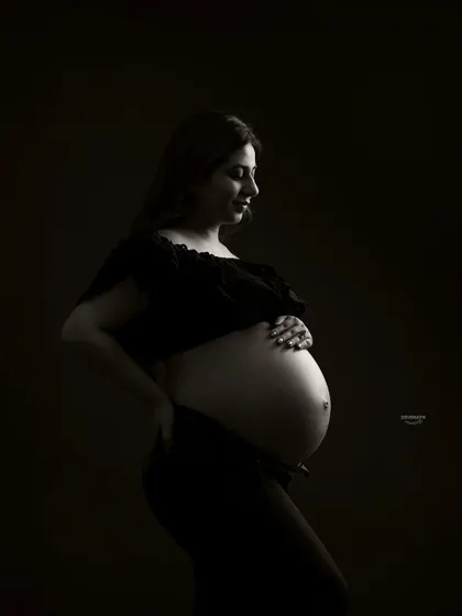 A classic low-key bare-bump profile shot. This style uses dramatic shadows to create a powerful and intimate portrait, focusing on the beautiful curves of pregnancy.