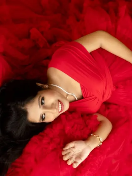 A joyful top-down portrait on a bed of red tulle. The smile and flowers in the hair add a touch of whimsy and happiness.