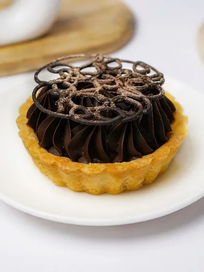 An artisanal chocolate tart with intricate piping and a dusting of cocoa, presented elegantly on a white plate.