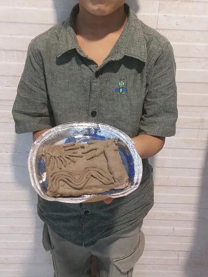 A child displays his clay relief sculpture. This activity teaches the basics of sculpting and allows for creative expression through a three-dimensional medium.