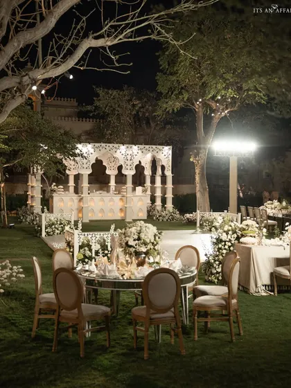 The full evening setup for the 'Sheesh Mahal' reception, with mirrored tables reflecting the candlelit structures and surrounding trees.