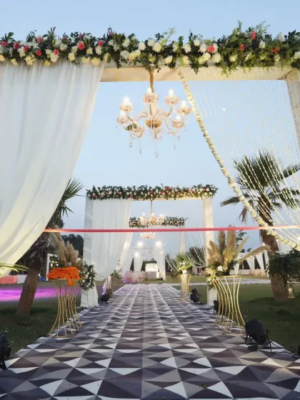 A grand entrance for an outdoor wedding, featuring a floral archway, elegant chandeliers, and a striking geometric-patterned aisle runner.