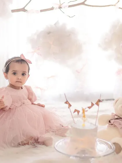 A classic first birthday portrait with a cake and teddy bear. The baby's direct gaze and the soft, dreamy background make this a timeless milestone photo.