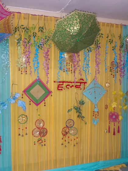 A colorful Haldi backdrop with yellow and light blue drapes. The decor features hanging umbrellas and various traditional ornaments for a fun and festive look.
