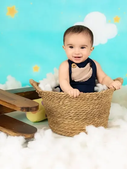 A happy baby boy sits in a basket amidst clouds and a toy airplane, ready for a magical journey.