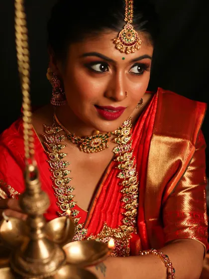 This Kemp jewelry set, with its vibrant red and green stones, is perfect for a classic bridal look. The set includes a choker, a longer haram with a large pendant, and a matching maang tikka, shown here by the warm light of a traditional lamp.