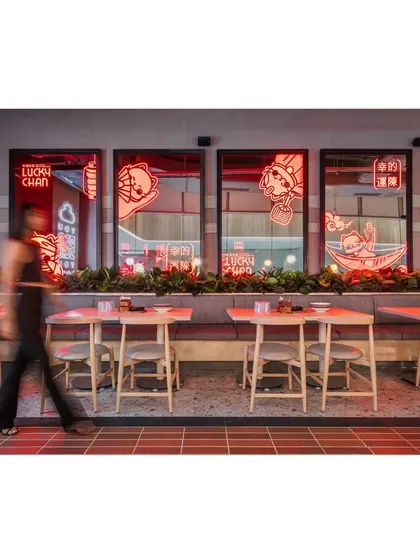 A person walking past the neon-lit windows adds a sense of movement and life to the space. The design is intended to be a dynamic backdrop for the activity of the restaurant.