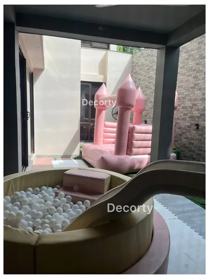 A fun play area with a ball pit and a pink inflatable bouncy castle, perfect for a rainbow or princess-themed party.