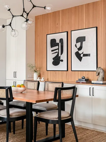 A dining room from 2023, featuring a wood-paneled wall, modern black and white art, and classic cane chairs. A great example of our eclectic, collected aesthetic.