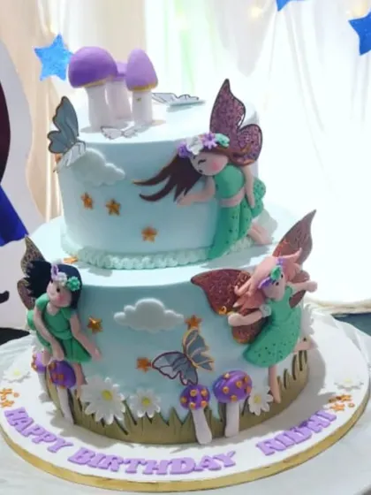 A lovely two-tiered cake with a fairy garden theme. It features delicate, handcrafted fairies, mushrooms, and butterflies in a soft color palette.