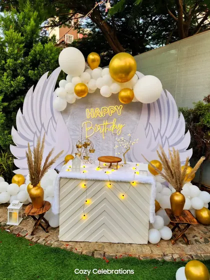 An angelic "heaven sent" theme in a garden setting. The large angel wings backdrop, white and gold balloons, and pampas grass create a serene and beautiful photo spot.