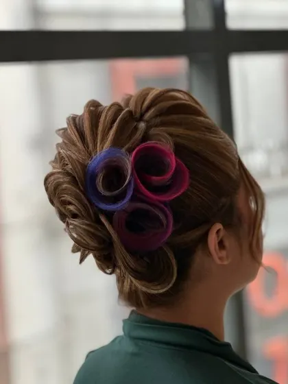 A creative and colorful updo featuring rolled sections of hair in pink and blue. This demonstrates how to incorporate color and avant-garde shapes into hairstyling.