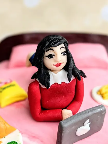 This fondant figurine was created for a foodie who loves watching shows in bed. I sculpted her with her laptop, surrounded by her favorite snacks.