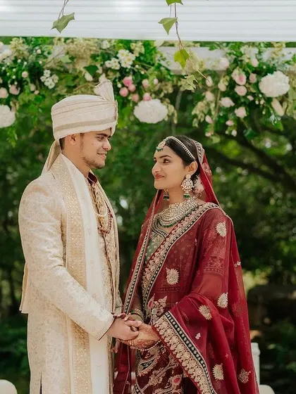 A couple shares a look of love, holding hands under a beautiful floral mandap.